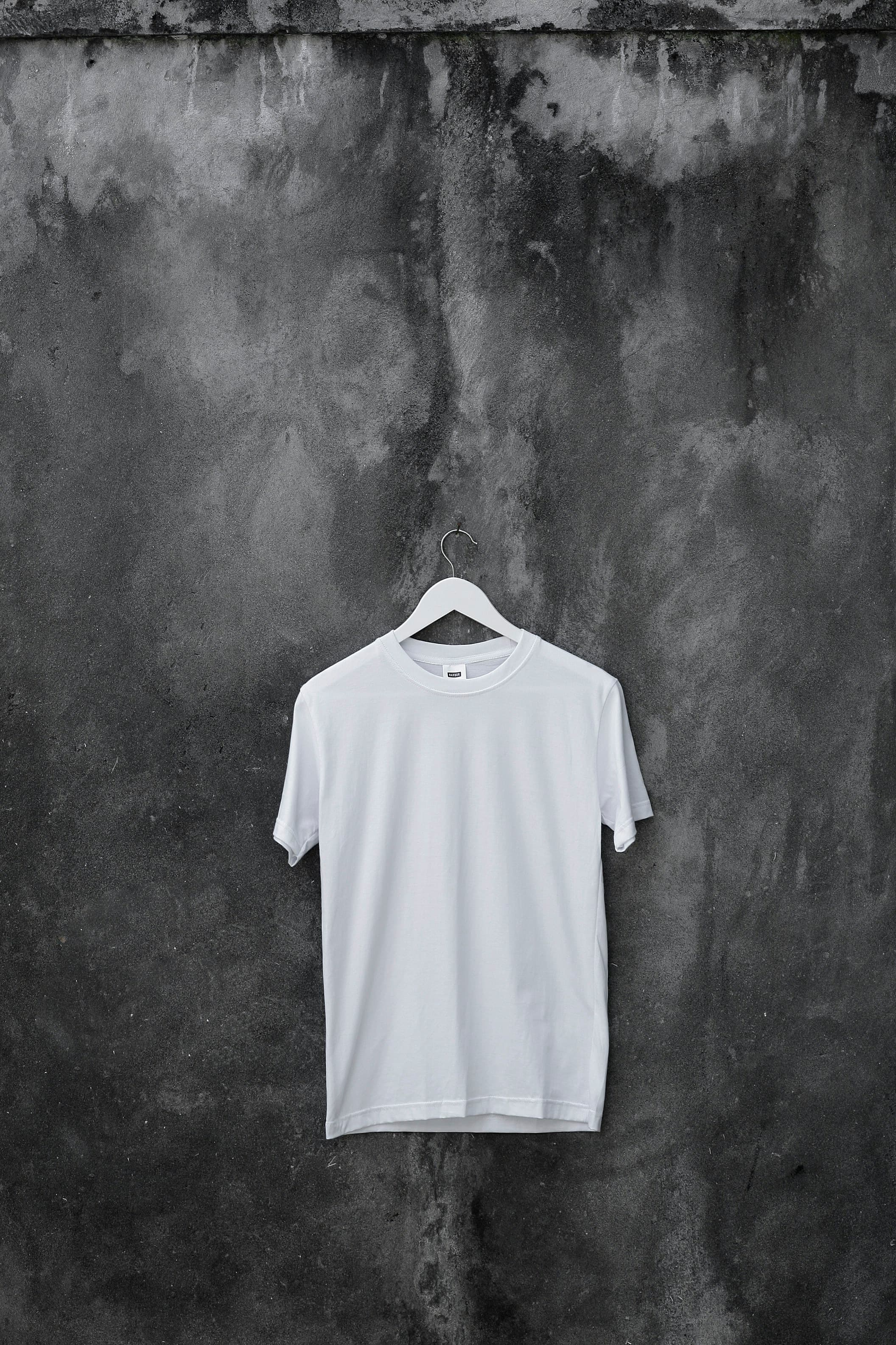 White crew-neck T-shirt on a hanger against a concrete wall